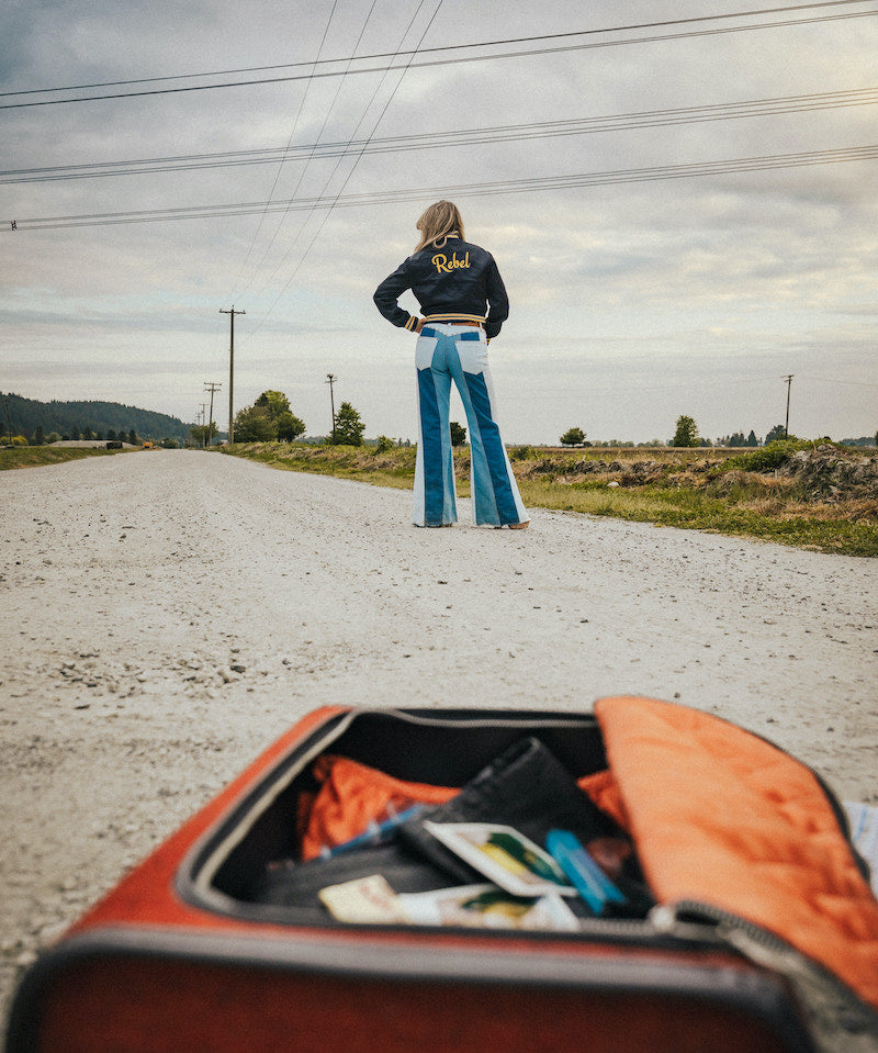 Person standing on a road with an open suitcase in the foreground wearing Soul Sister since 1969