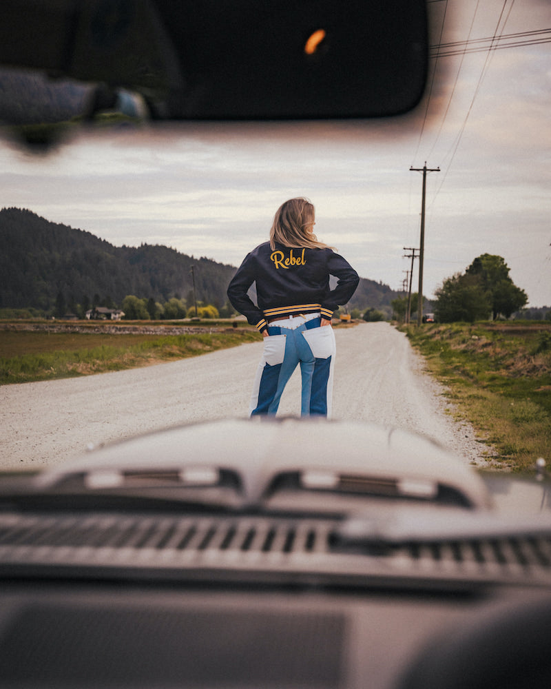 Person standing on a road with mountains in the background, viewed from inside a vehicle wearing Soul Sister since 1969.