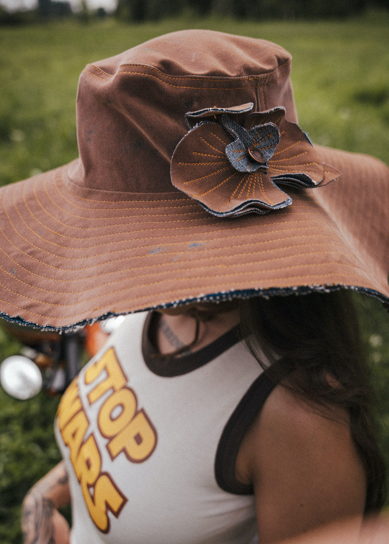 Person wearing a brown hat with a decorative flower, partially visible, in an outdoor setting. Designed by Soul Sister since 1969