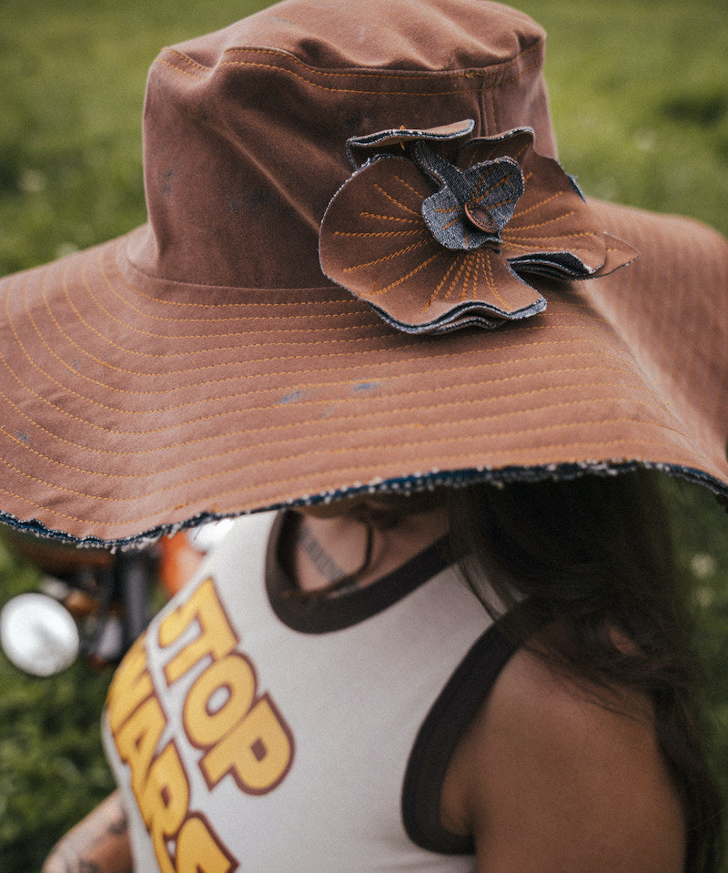 Person wearing a brown hat with a decorative flower, partially visible, in an outdoor setting. Designed by Soul Sister since 1969
