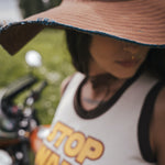 Person wearing a tank top with 'STOP WARS' text, standing outdoors wearing an oversized hat 
