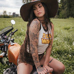 Woman with tattoos sitting on a motorcycle in a field wearing a hat and clothing Designed by Soul Sister since 1969