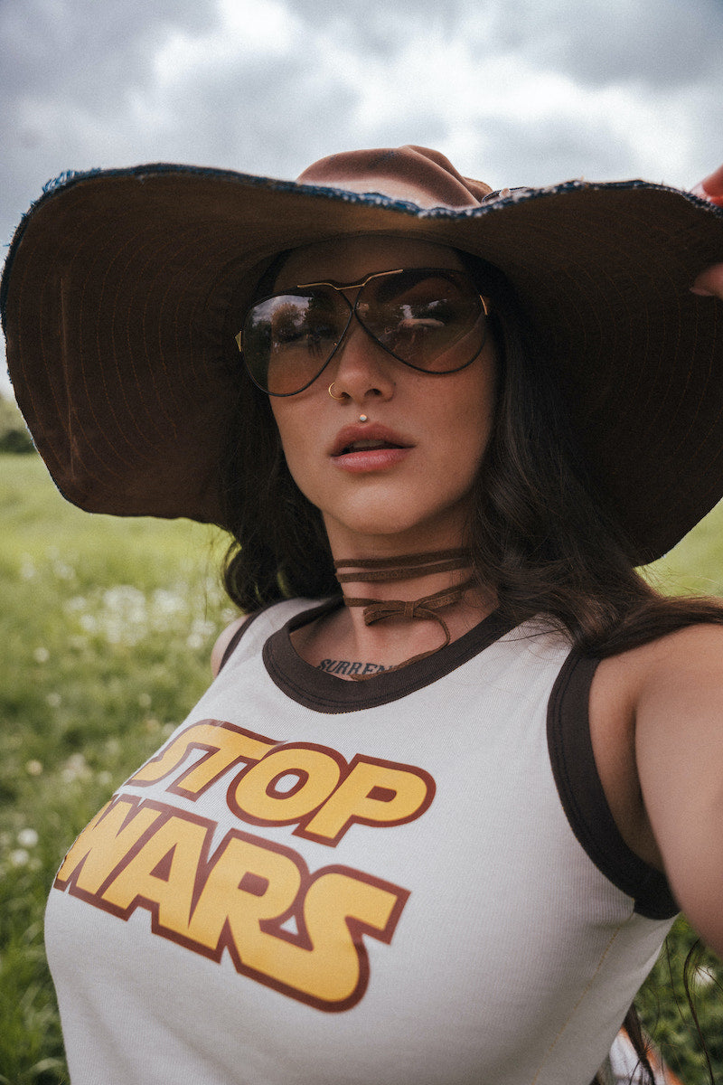 Person wearing a 'Top Wars' tank top and large hat in a field. Designed by Soul Sister since 1969