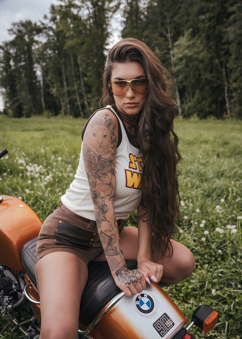 Woman with tattoos sitting on a motorcycle in a field wearing clothing designed by Soul Sister since 1969