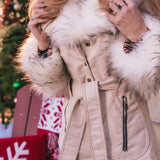 Person wearing a beige Penny lane vintage 70s inspired coat with white fur trim in a festive setting.