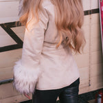Person wearing a beige Penny Lane coat with fur cuffs and black leather pants, standing in front of a wooden wall.