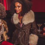 Woman wearing a fur-trimmed coat in a bar setting with a cocktail in the background
