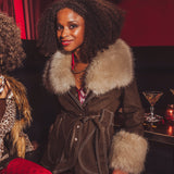 Woman wearing a fur-trimmed coat in a bar setting with a cocktail in the background