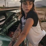 Woman leaning on a car with an open hood in a rural setting wears clothing by Soul Sister since 1969