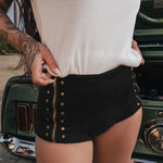 Person wearing a white top and black shorts with gold buttons, standing next to a vintage car wears clothing by Soul Sister since 1969.