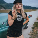 Woman in black cap and t-shirt standing next to a vintage car on a road with mountains in the background Ride or Die Motor Club wearing soul sister since 1969