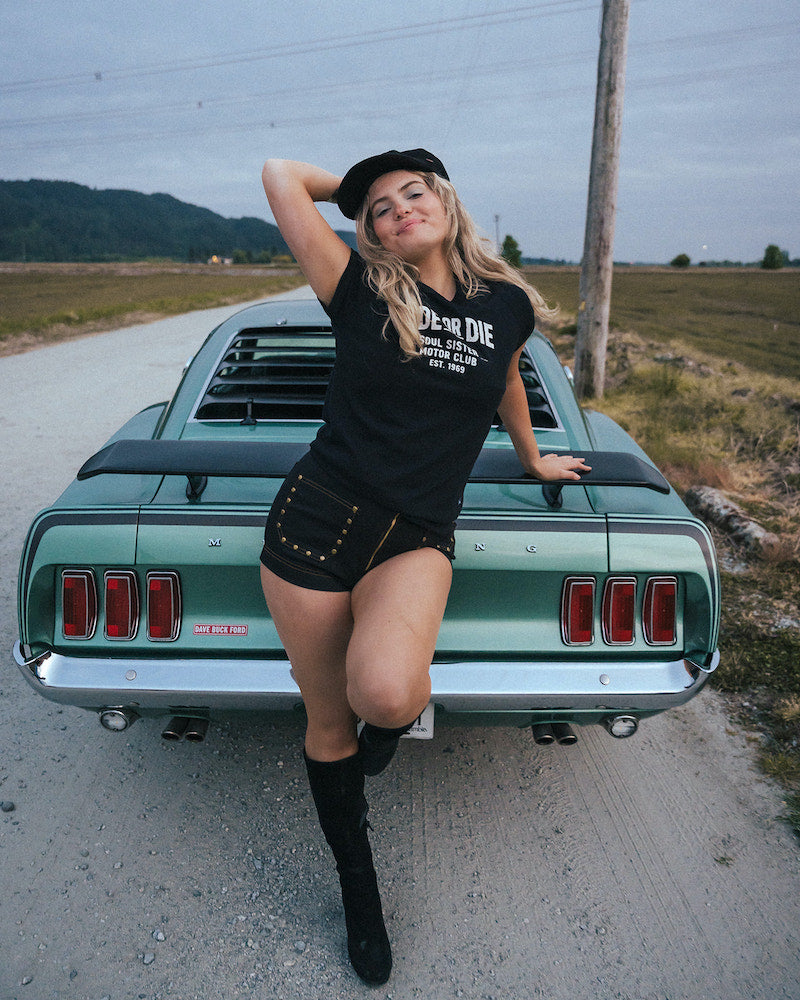 Woman posing on a classic car in a rural setting