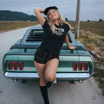 Woman posing on a classic car in a rural setting