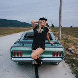 Woman posing on a classic green car in a rural setting