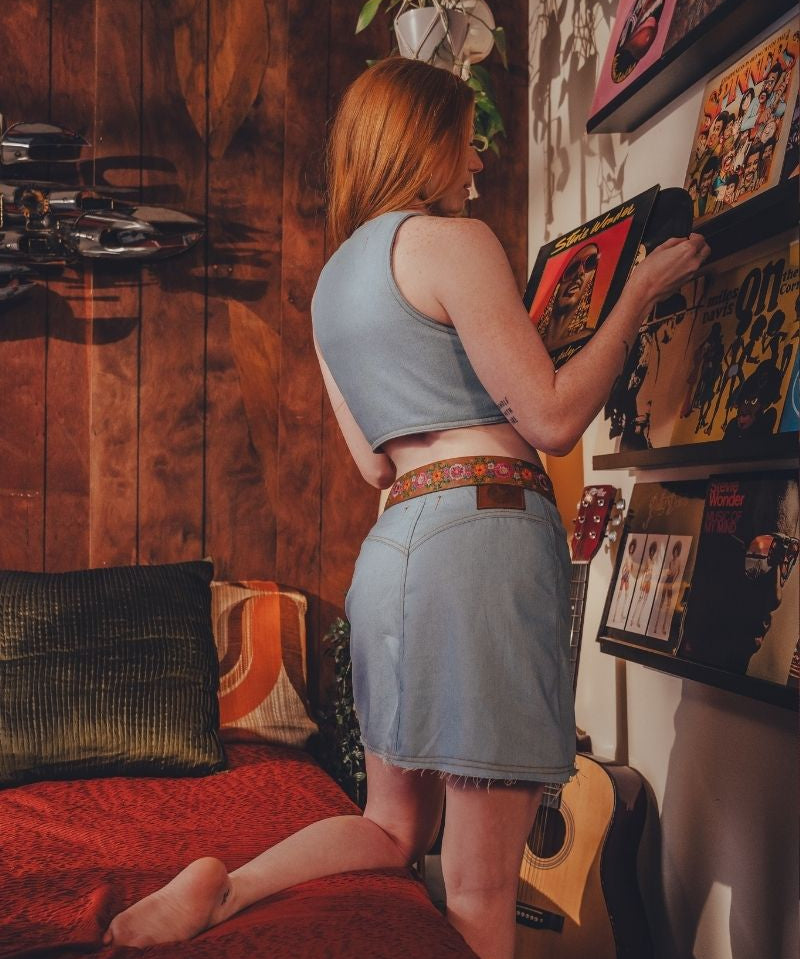 Woman in a casual outfit standing in a room with a guitar and shelves.