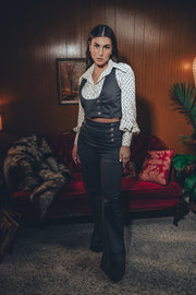 woman leans against a vintage sideboard wearing a black 70's style suit in a cozy retro interior
