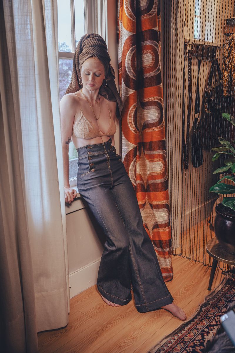 Woman in a room with a patterned curtain and wooden floor.