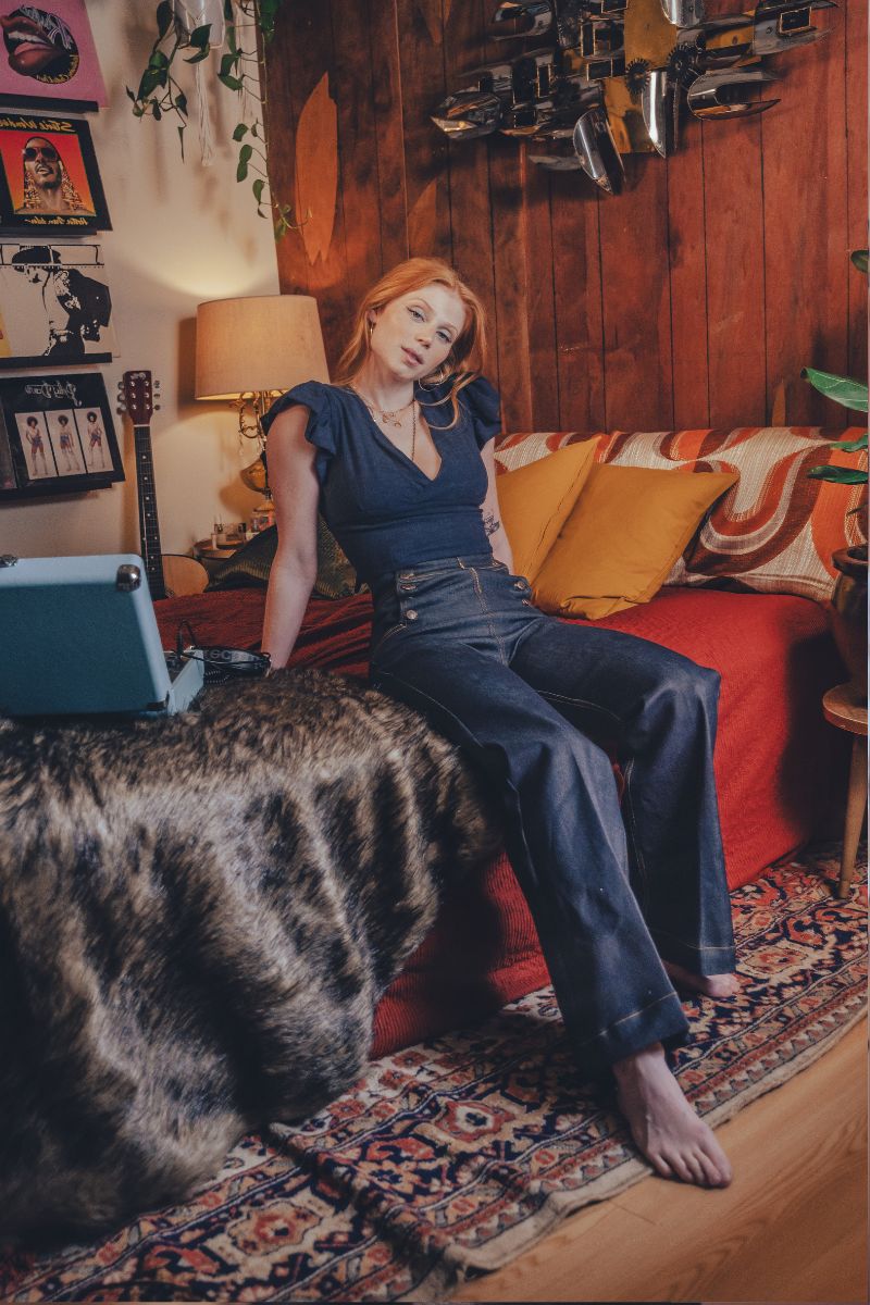 Woman sitting on a couch in a cozy living room with a laptop.