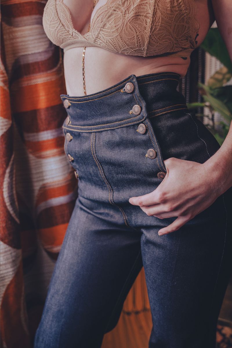 Person wearing a beige lace top and high-waisted blue jeans with a blurred background