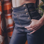 Person wearing a beige lace top and high-waisted blue jeans with a blurred background