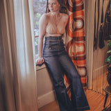 Woman in a beige top and dark pants standing by a window with colorful curtains.