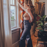 Woman in a stylish outfit standing by a window in a room with decorative elements.