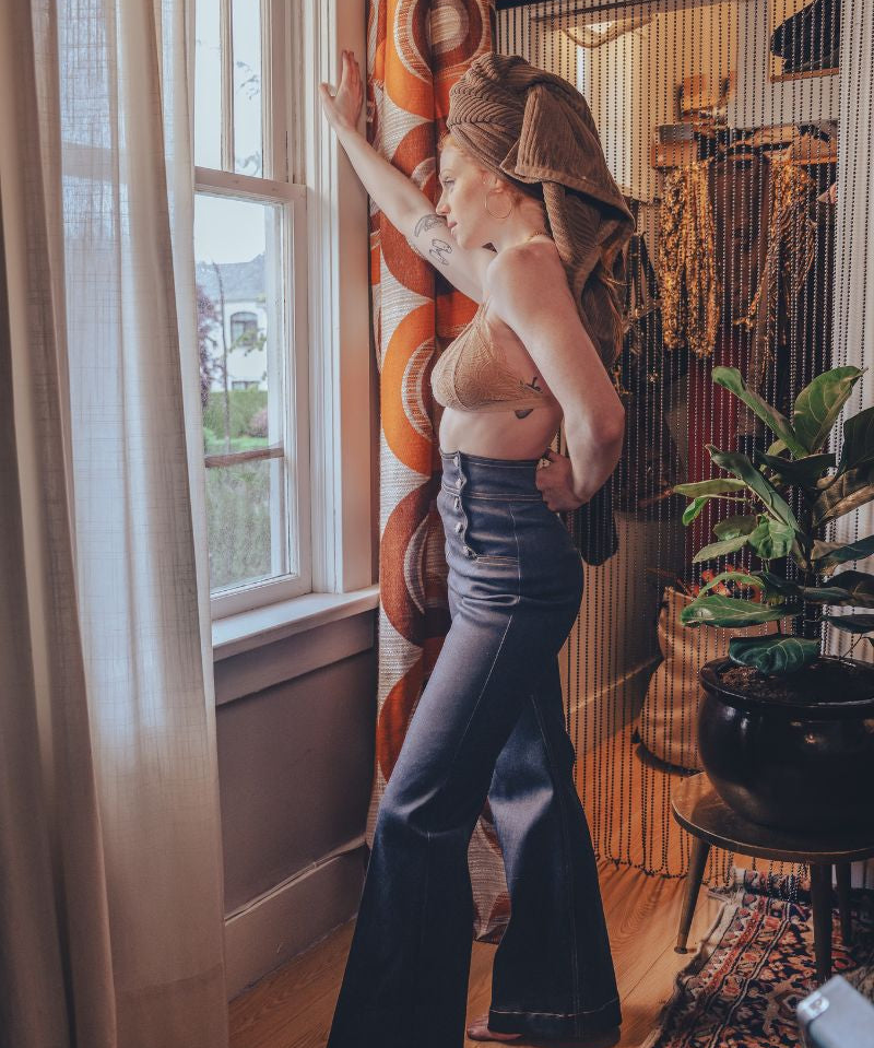 Woman in a stylish outfit standing by a window in a room with decorative elements.