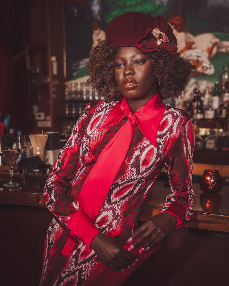 Woman in a stylish outfit with a red tie and patterned coat in a bar setting