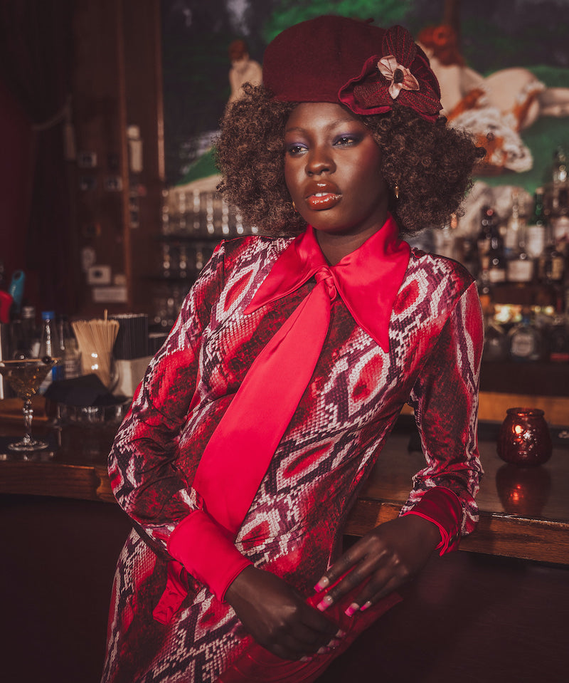 Woman in a stylish outfit with a red tie and patterned coat in a bar setting
