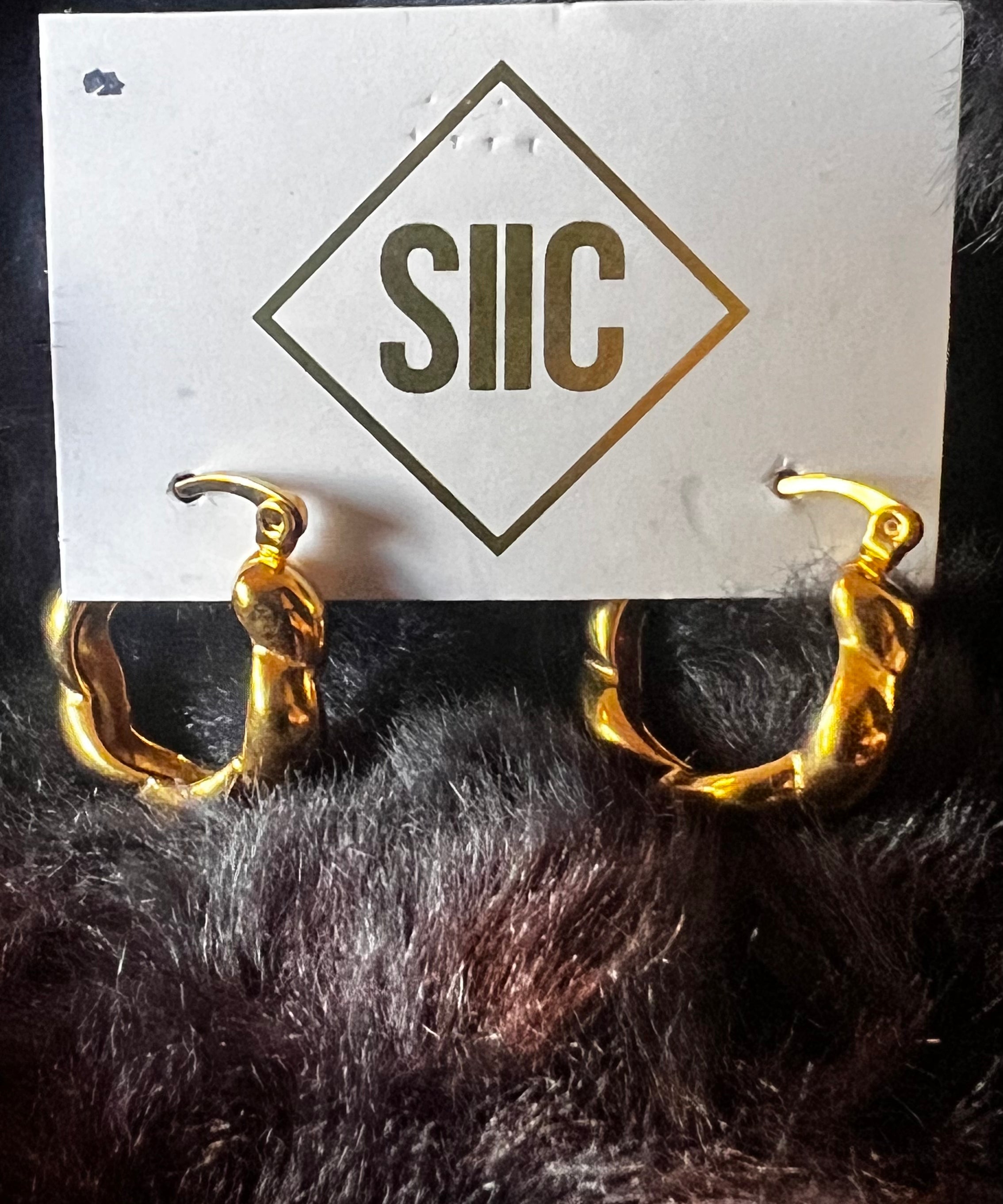Gold hoop earrings on a card with 'SIIC' branding against a dark background