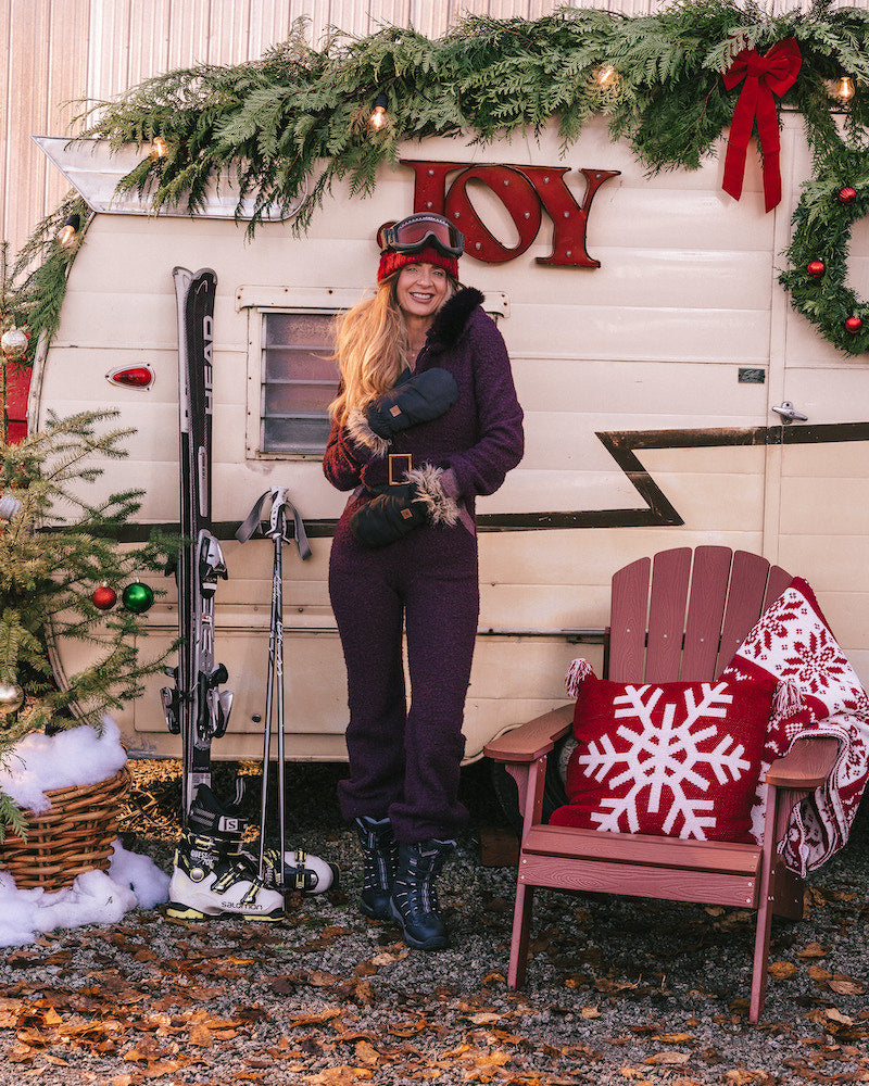 Person in winter clothing standing in front of a decorated trailer with 'JOY' and Christmas decorations.