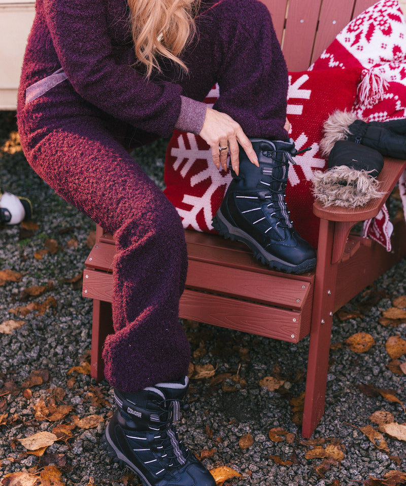 Person sitting on a red chair wearing dark purple pants and black boots, with a red and white patterned blanket.