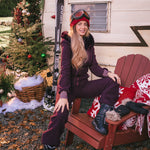 Woman in ski gear sitting on a red chair in front of a trailer with 'JOY' decoration and Christmas tree.