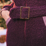 Close-up of a person wearing a purple coat with a gold buckle, blurred background