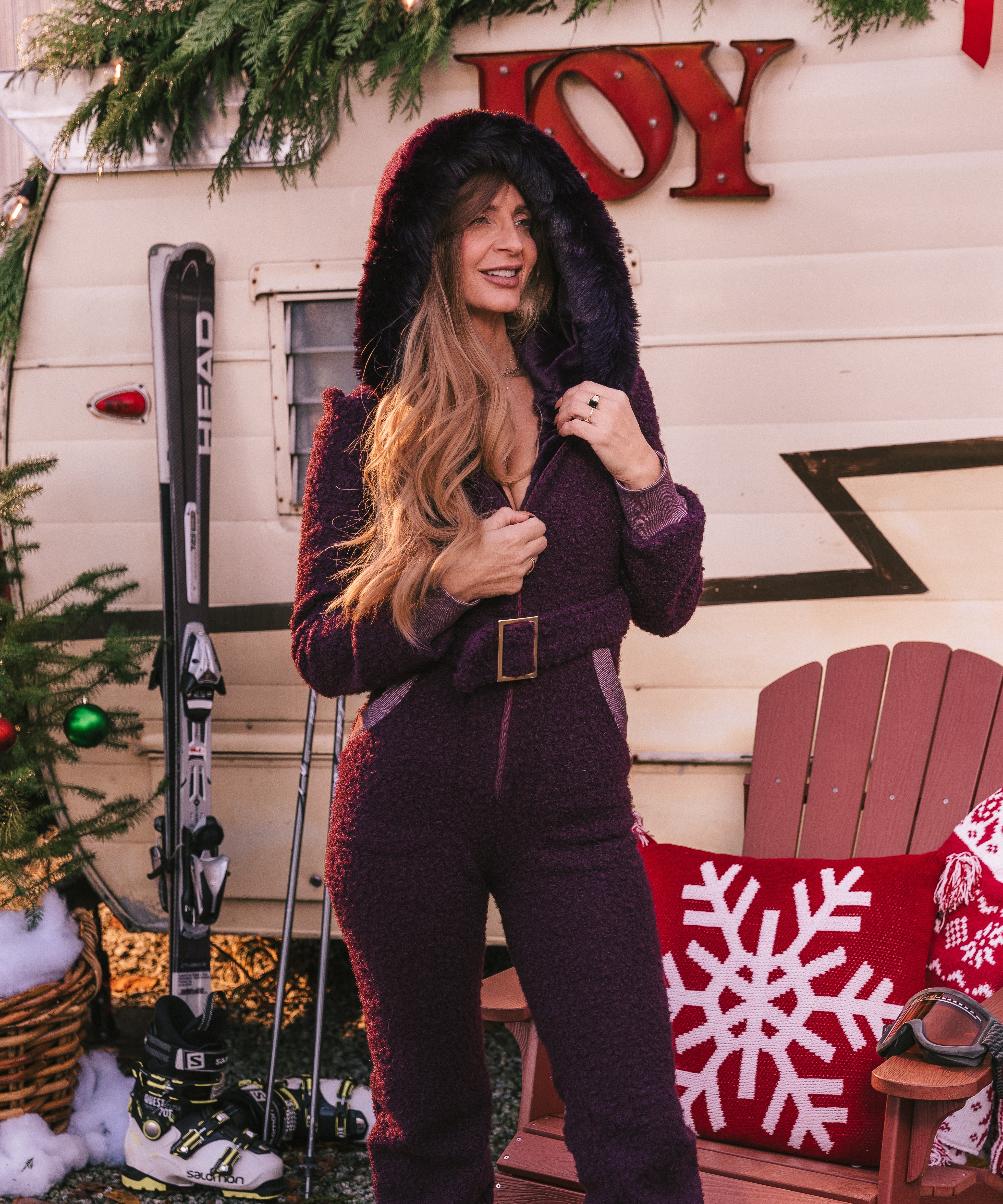 Woman in a purple outfit standing in front of a Christmas-themed trailer with skis and a chair.