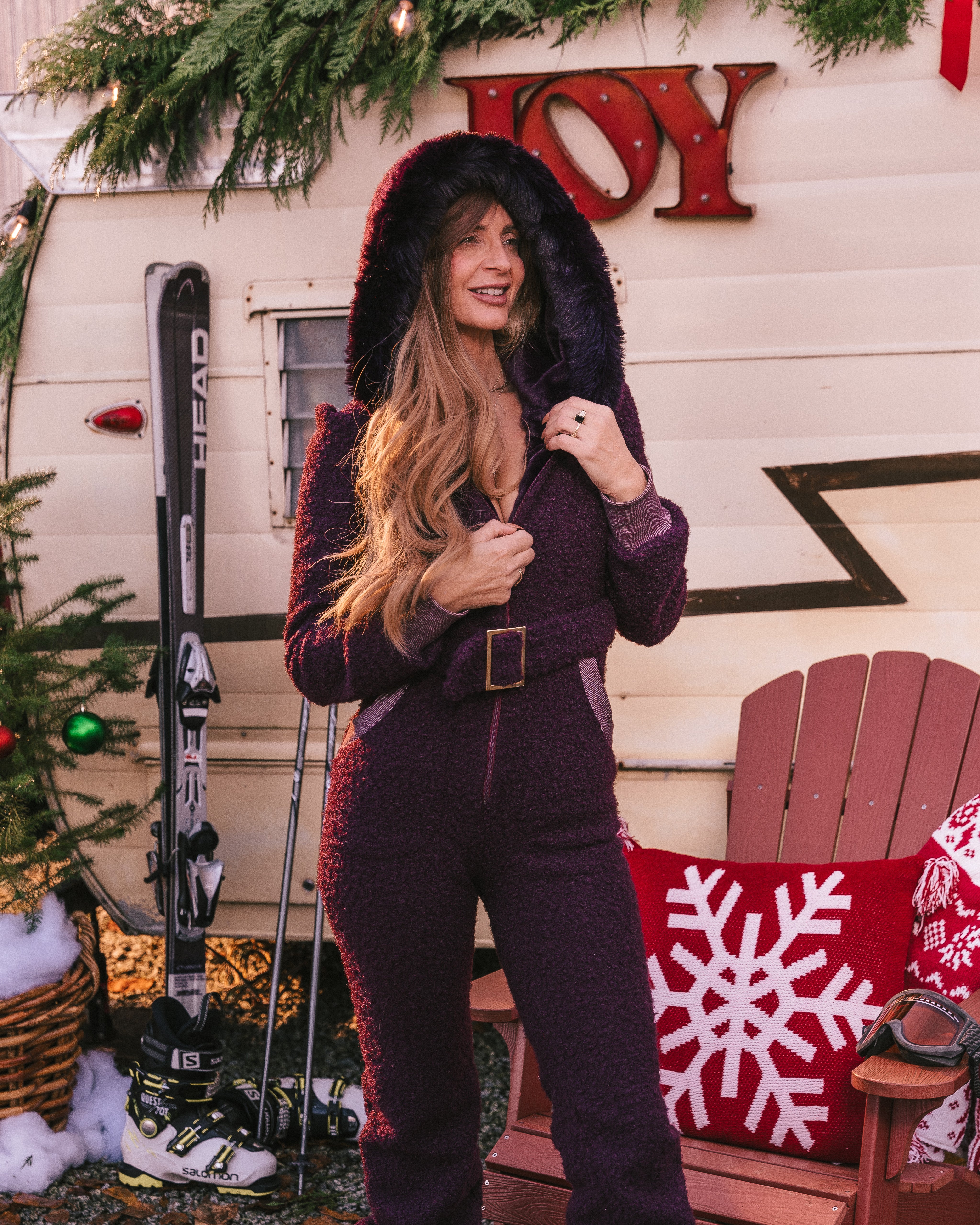 Woman in a purple outfit standing in front of a Christmas-themed trailer with skis and a chair.