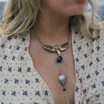 Close-up of a woman wearing a gold necklace with a butterfly pendant and black beads wearing Soul Sister since 1969..