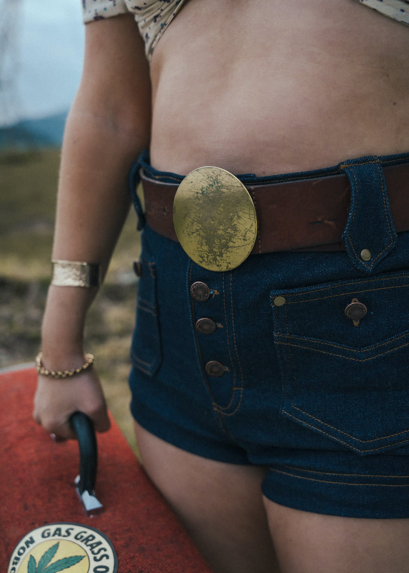 Person wearing a gold belt buckle and denim shorts with a blurred background wearing Soul Sister since 1969.
