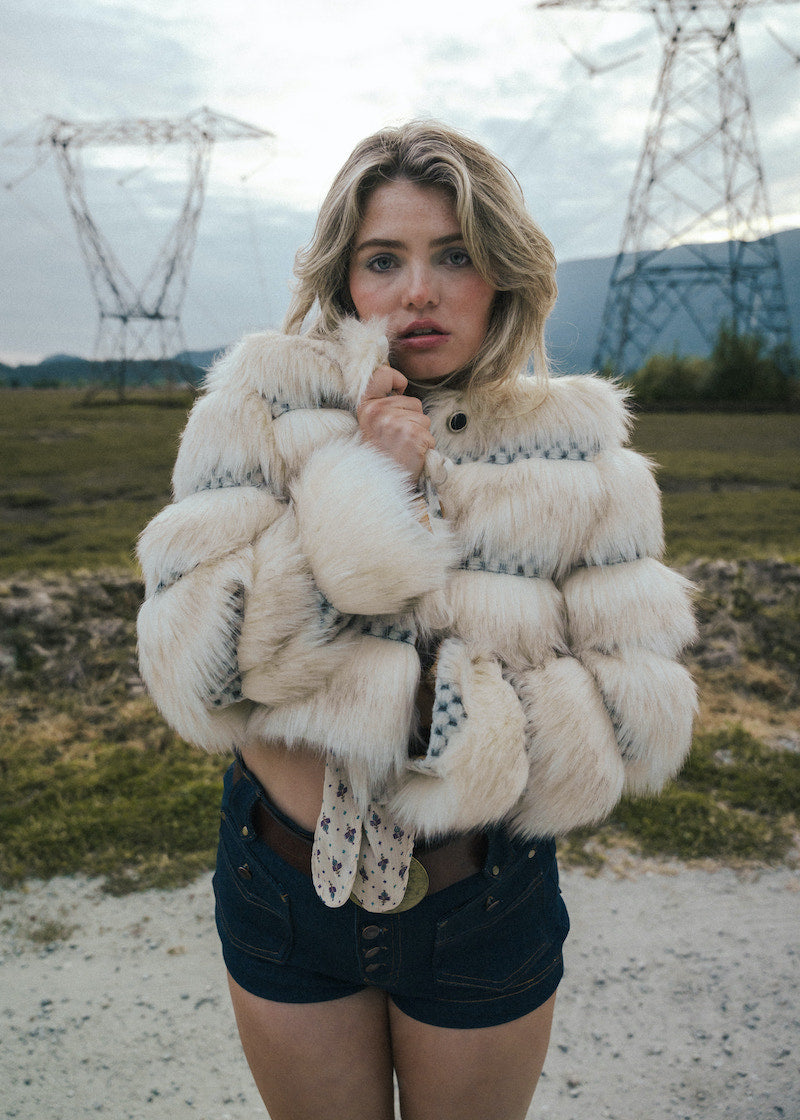 Woman wearing a fluffy white jacket in an outdoor setting with power lines in the background wearing Soul Sister since 1969
