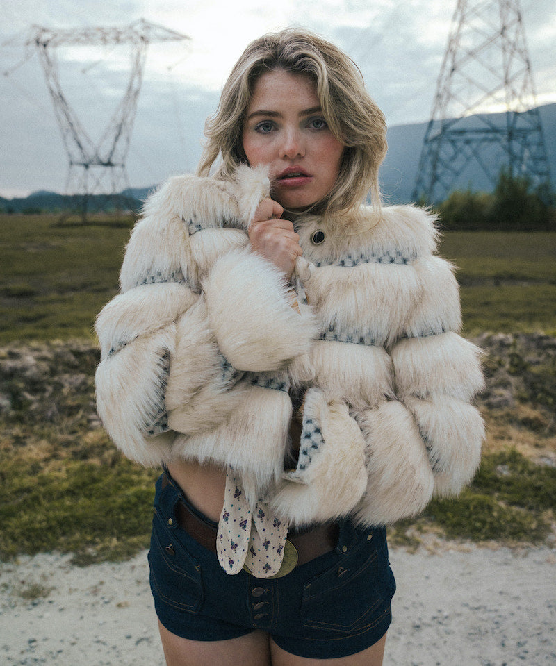 Woman wearing a fluffy white jacket in an outdoor setting with power lines in the background wearing soul sister since 1969