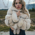 Woman wearing a fluffy white coat and gloves in an outdoor setting with power lines in the background wearing soul sister since 1969