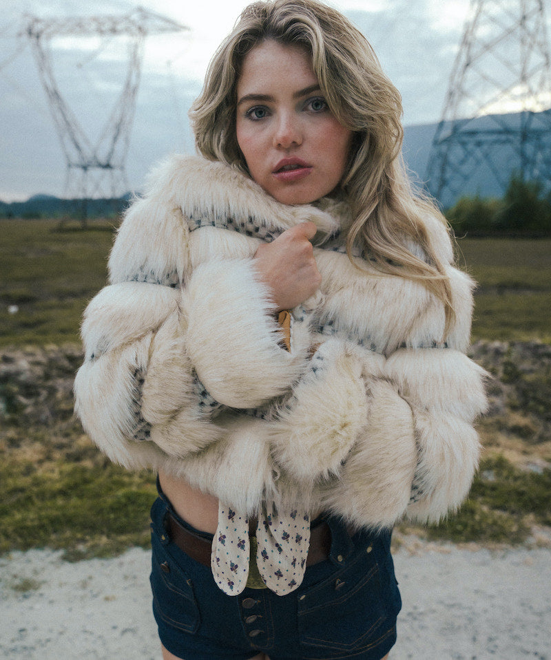 Woman wearing a fluffy white coat and gloves in an outdoor setting with power lines in the background wearing soul sister since 1969