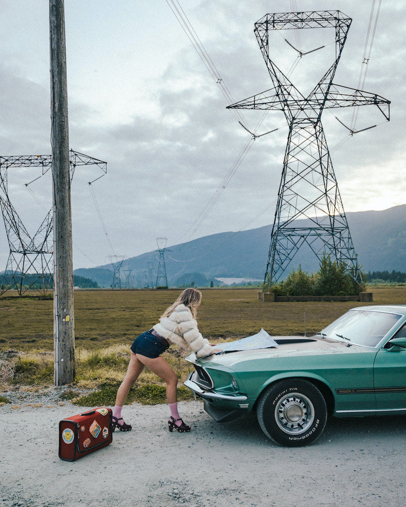 Person leaning against a vintage car with power lines and mountains in the background wearing soul sister since 1969