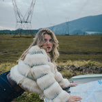 Woman in a fur coat looking at a map next to a car in a scenic outdoor setting wearing soul sister since 1969.