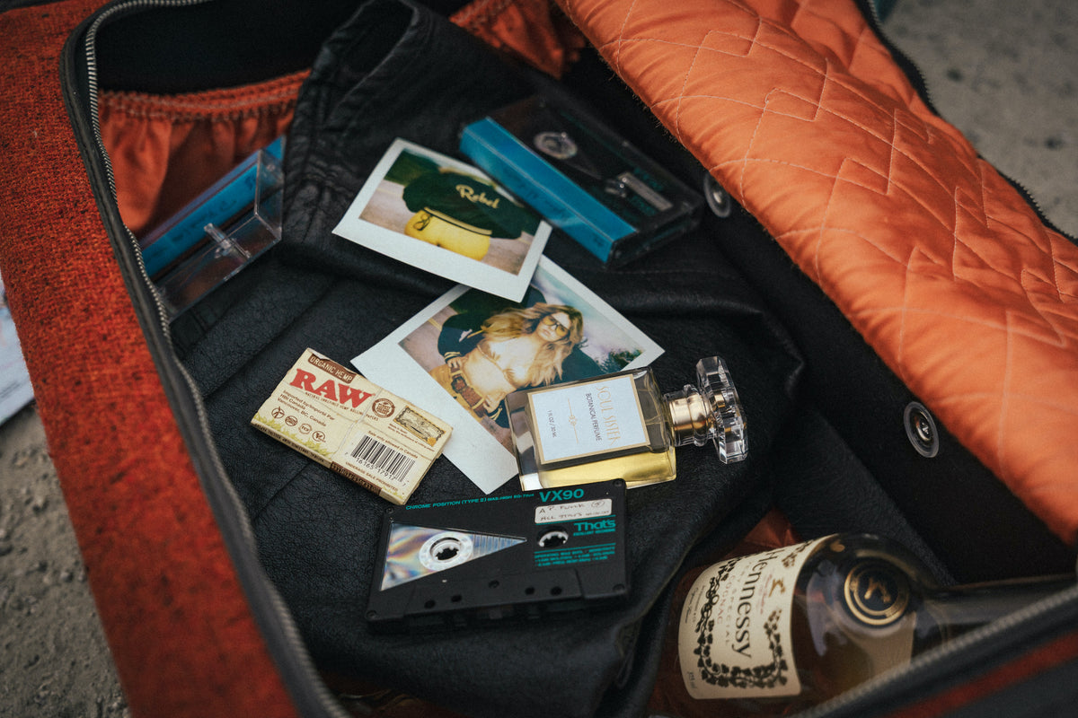 Open Soul Sister suitcase with items including a bottle of whiskey, photos,  tapes and Soul Sister botanical perfume mist.
