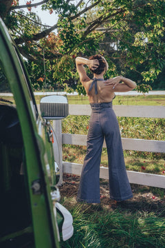 A person posing by a fence wearing high waisted bell bottoms and a sleeveless top.