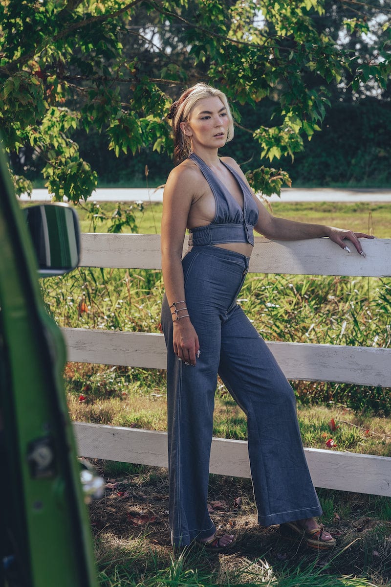 A person posing by a fence wearing high waisted bell bottoms and a sleeveless top.