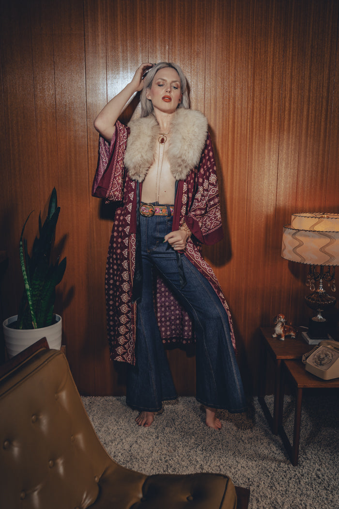 Bellbottom jeans are worn by a model in a retro styled 1970s living room

