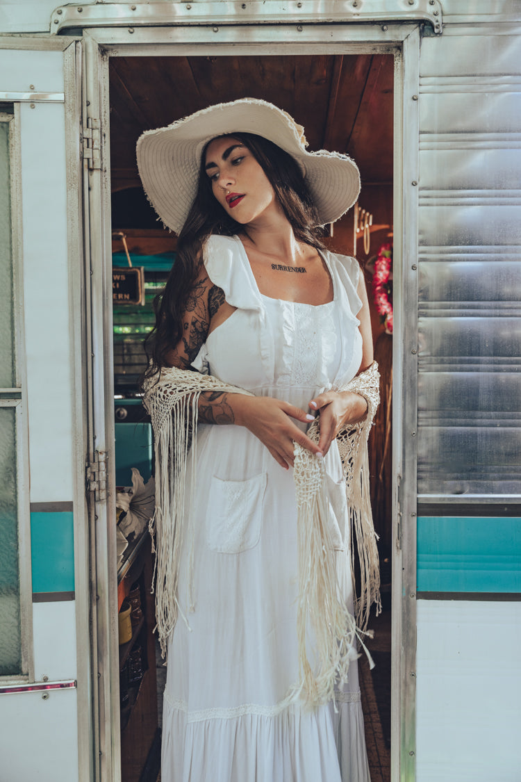 Soul Sister since 1969 long white dress on beautiful woman with a fringe shawl and retro floppy hat standing in a vintage trailer