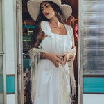 Soul Sister since 1969 long white dress on beautiful woman with a fringe shawl and retro floppy hat standing in a vintage trailer